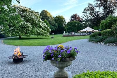 Miniature Location salle Namur (Namur) - Château de Beez #19 Groupe de personnes assises en extérieur lors d'une cérémonie, entourées d'arbres et de fleurs sous un ciel partiellement…