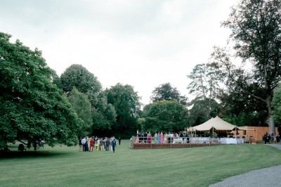 Miniature Location salle Namur (Province de Namur) - Château de Beez #28 Groupe de personnes rassemblées sous une tente beige sur une terrasse en bois, dans un jardin arboré.