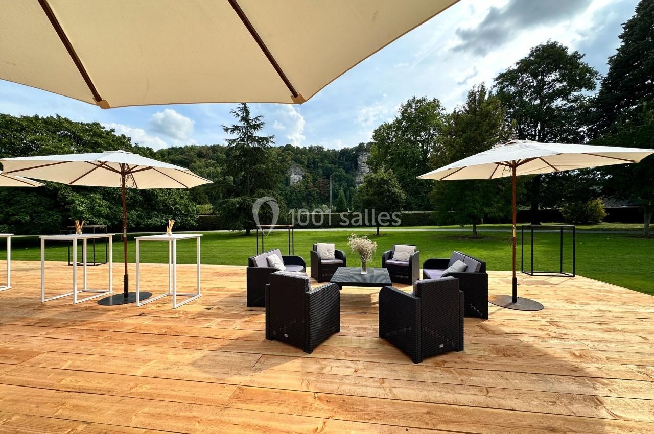 Terrasse en bois avec mobilier de jardin, parasols et vue sur un parc verdoyant par une journée ensoleillée.