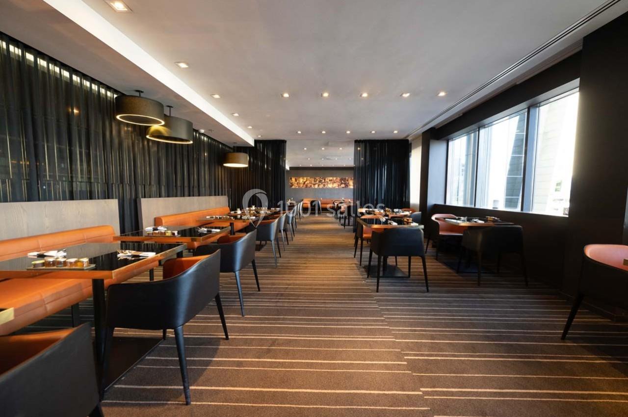 Salle de restaurant moderne avec tables dressées, chaises en cuir et grandes baies vitrées laissant entrer la lumière…