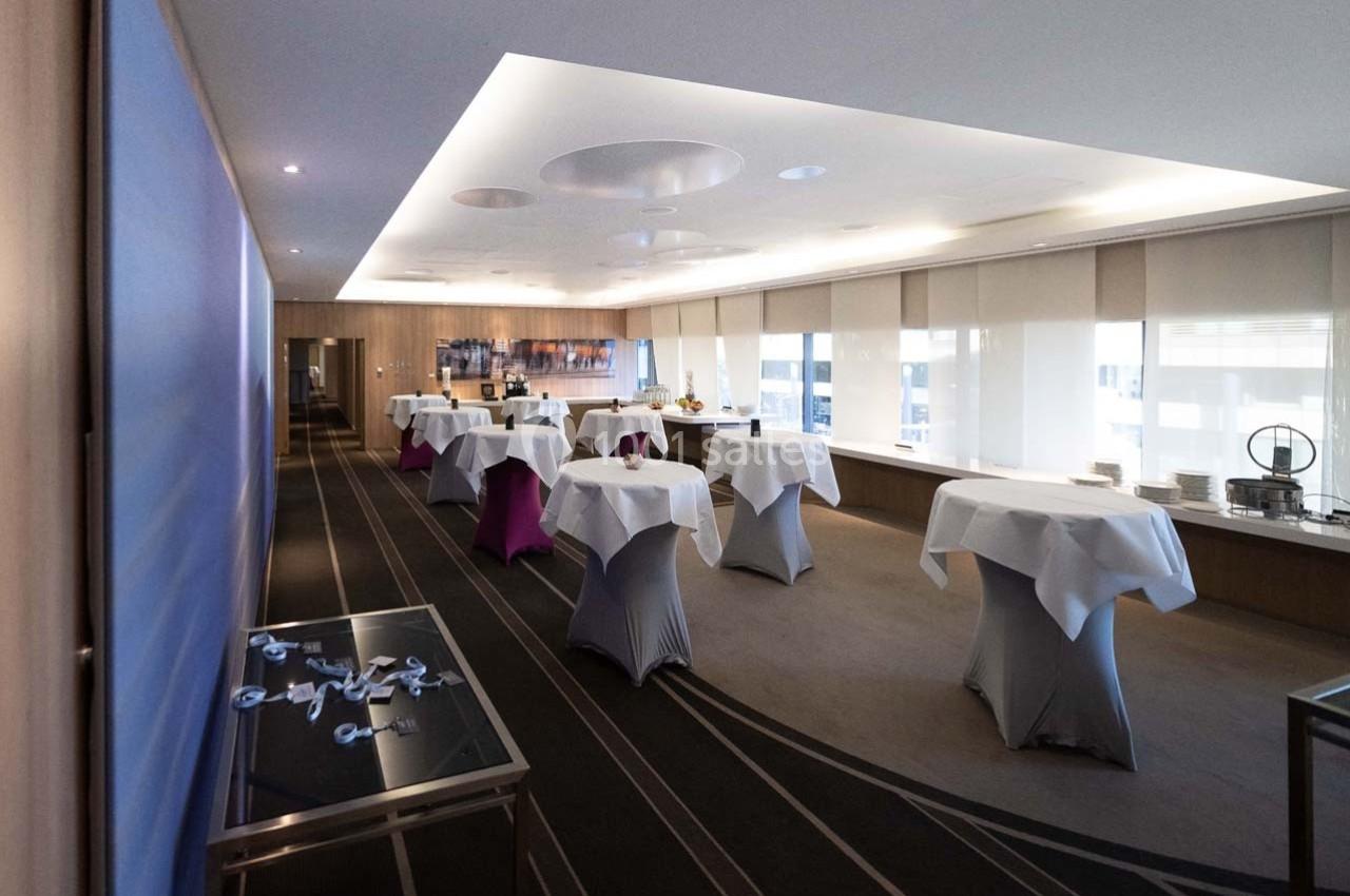 Salle de réception lumineuse avec des tables recouvertes de nappes blanches, prête pour un événement.