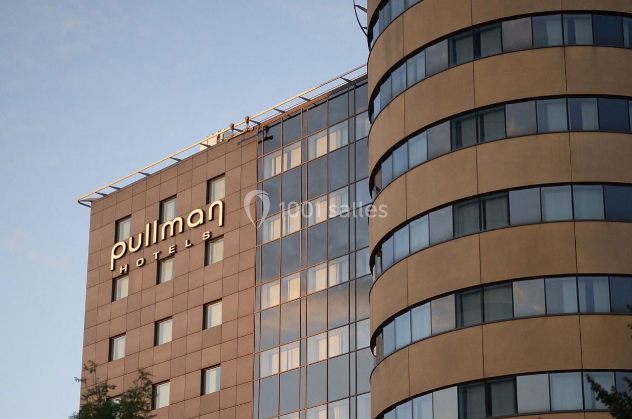 Façade d'un hôtel moderne avec le logo ’Pullman Hotels’ visible sur un mur beige au coucher du soleil.