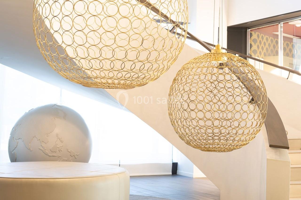 Deux suspensions dorées ajourées éclairent un espace moderne avec escalier et globe décoratif en arrière-plan.