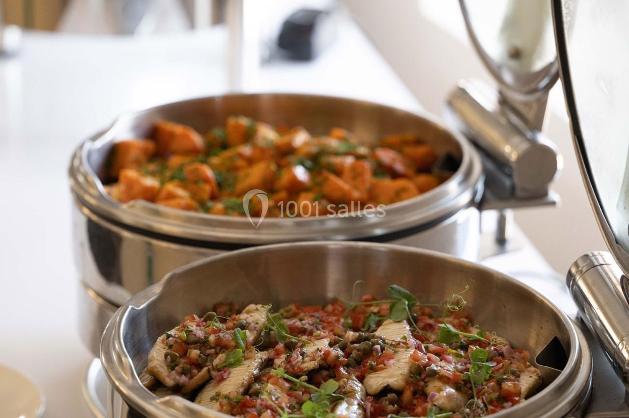 Plats chauds disposés dans des récipients en inox, comprenant des légumes et des viandes garnies d'herbes fraîches.