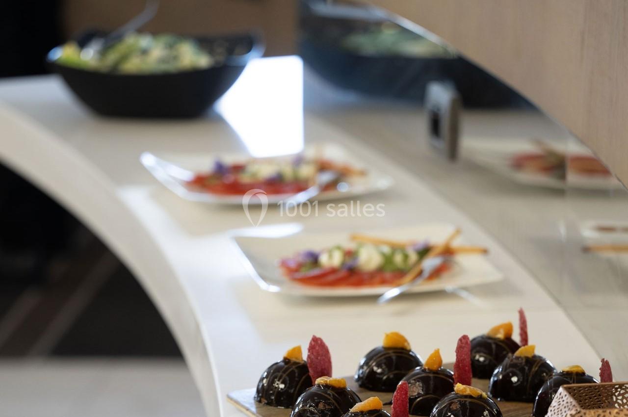 Desserts au chocolat décorés de fruits devant des assiettes de salades sur un comptoir blanc.