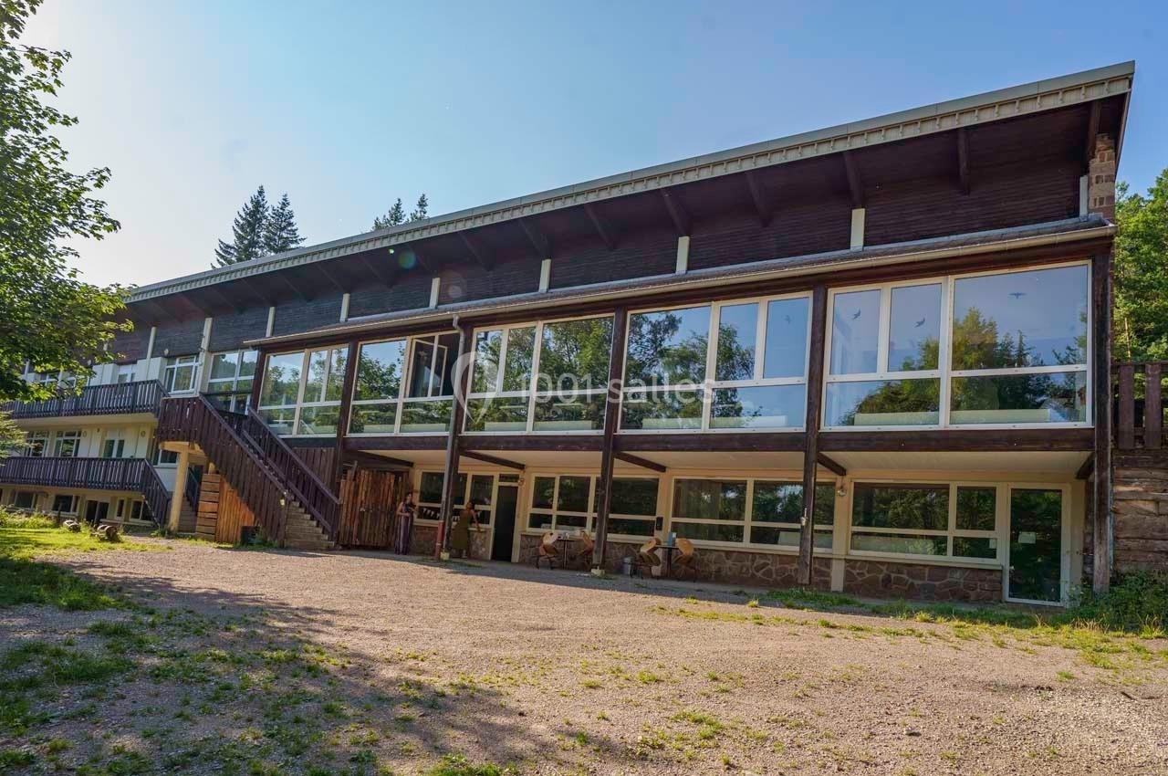 Bâtiment en bois avec de grandes baies vitrées, entouré de végétation, sous un ciel dégagé.