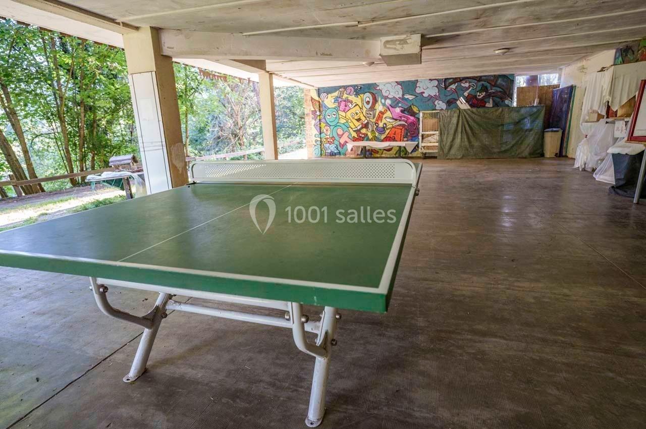 Table de ping-pong verte dans un espace couvert avec des murs décorés de graffitis colorés et une vue sur l'extérieur.