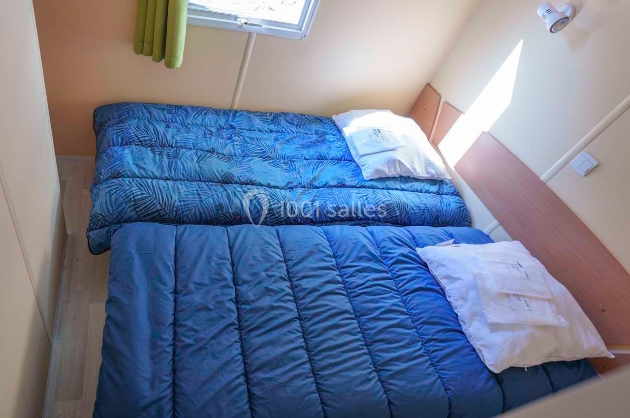 Deux lits simples avec des couettes bleues et des oreillers blancs dans une petite chambre lumineuse.