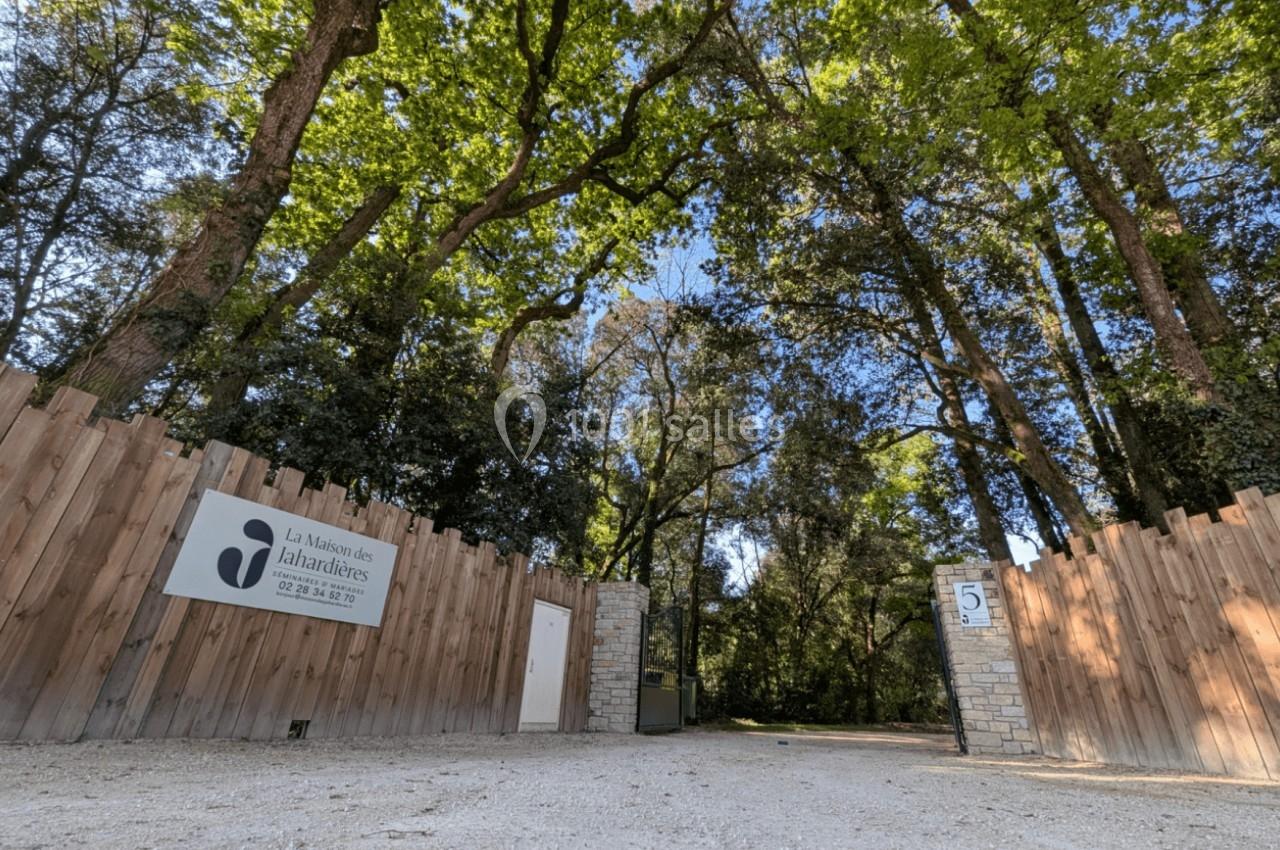 Entrée d'un domaine entouré d'arbres, avec une clôture en bois, un panneau et un portail ouvert.