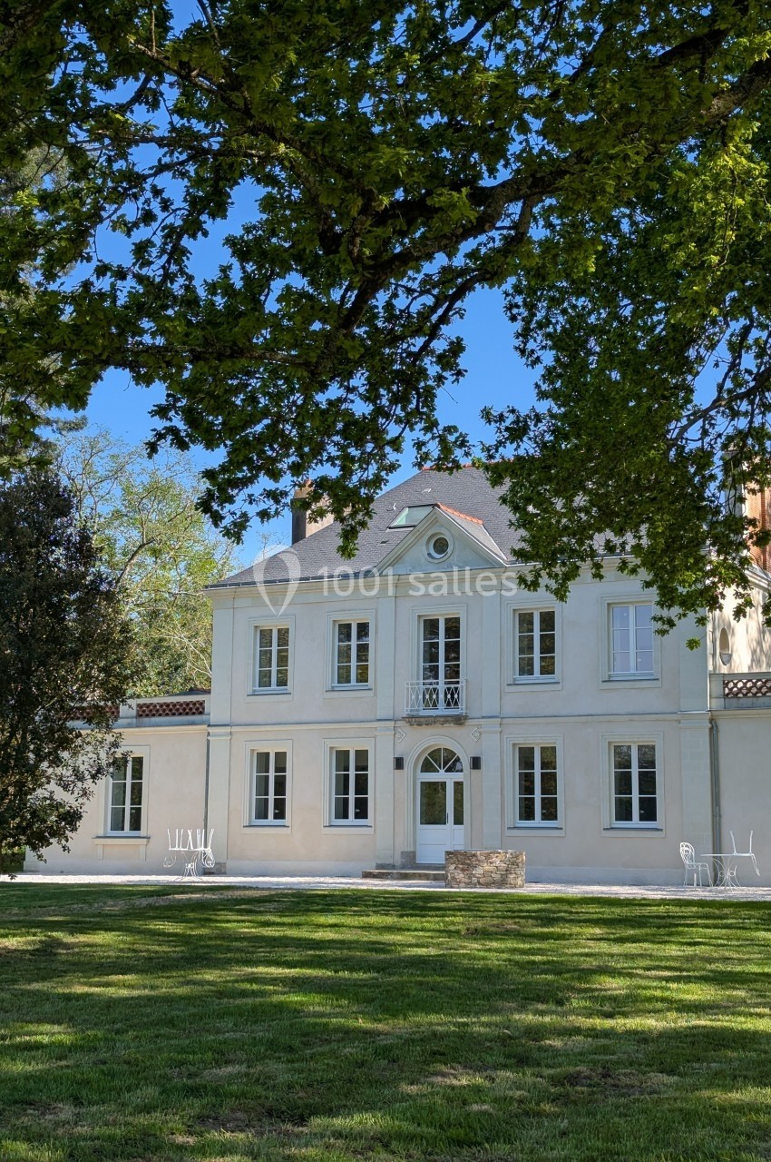 Façade d'une maison blanche à deux étages entourée d'arbres, avec une pelouse au premier plan.