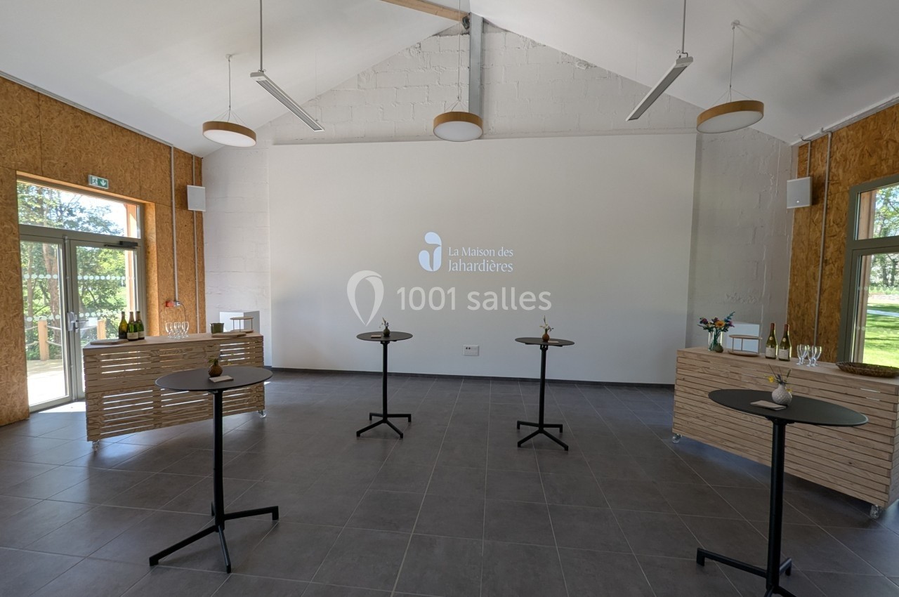 Salle lumineuse avec tables hautes, murs blancs, parquet gris et logo ’La Maison des Lahardières’ projeté au mur.