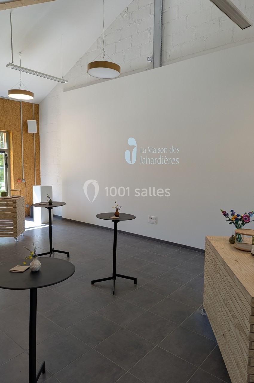 Salle lumineuse avec tables hautes, décor minimaliste, logo ’La Maison des Lahardières’ projeté sur un mur blanc.