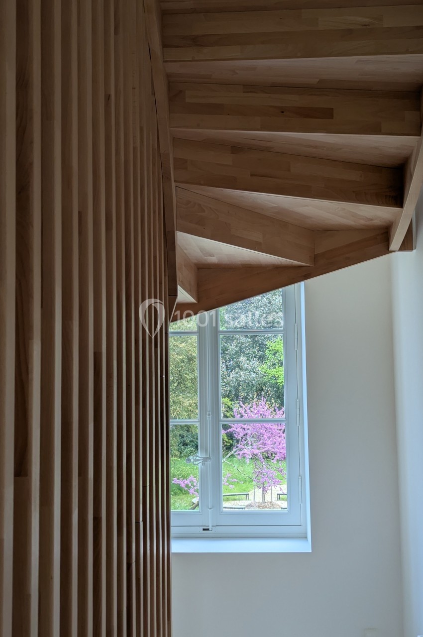 Escalier en bois avec des marches suspendues, près d'une fenêtre donnant sur un arbre en fleurs et un jardin.