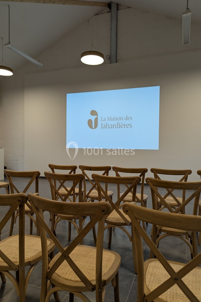 Salle avec des chaises en bois disposées face à un écran affichant le logo ’La Maison des Jahardières’.
