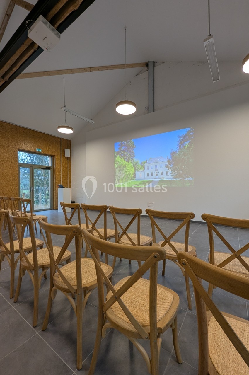 Salle de réunion avec des chaises en bois disposées face à un écran projetant l'image d'un bâtiment.