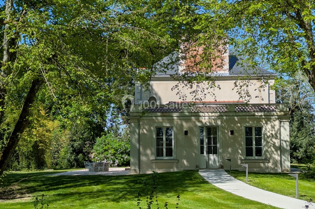 Maison claire entourée d'arbres et de pelouse, avec une allée menant à l'entrée principale.