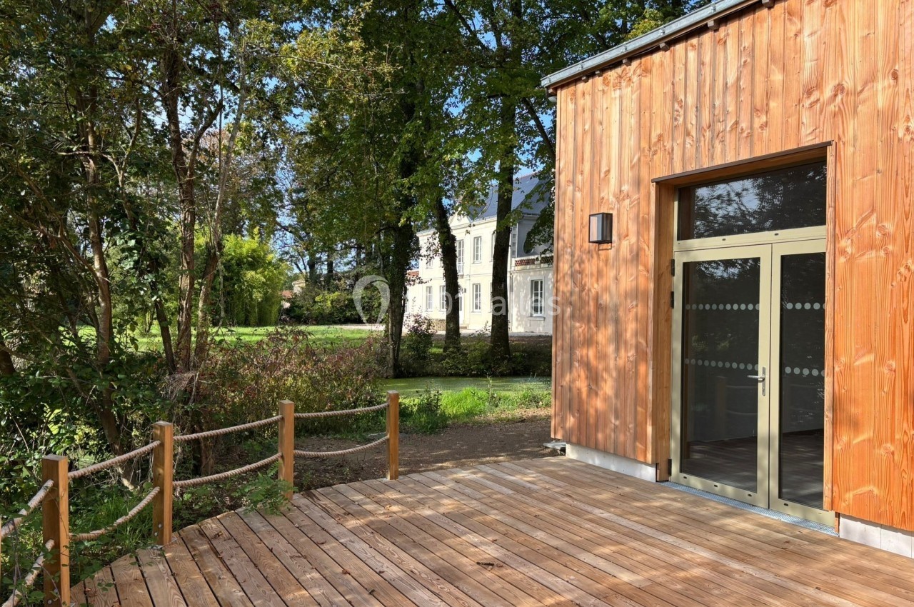 Terrasse en bois bordée de cordes, donnant sur un bâtiment en bois et un jardin arboré sous un ciel dégagé.