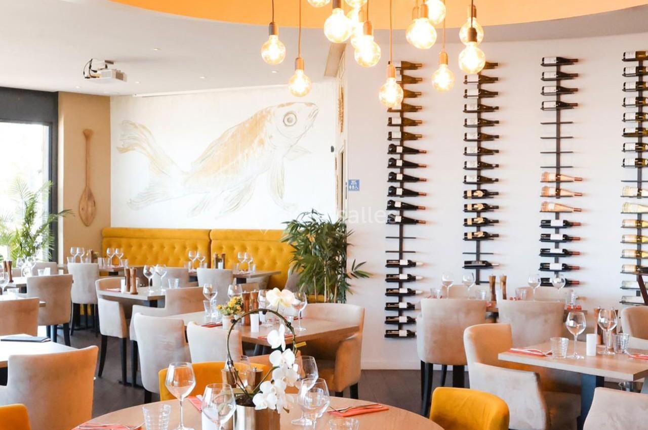 Salle de restaurant lumineuse avec tables dressées, décoration murale de couteaux et fresque de poisson.
