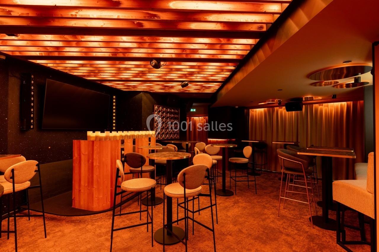 Salle de bar avec éclairage chaleureux, mobilier moderne et comptoir en bois sous un plafond lumineux.
