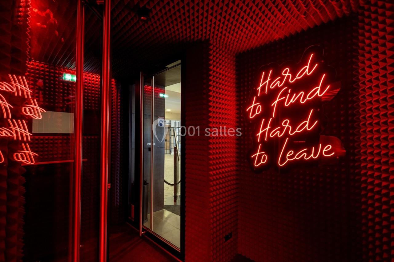 Mur rouge avec panneaux acoustiques et néon rouge affichant le message ’Hard to find, Hard to leave’.