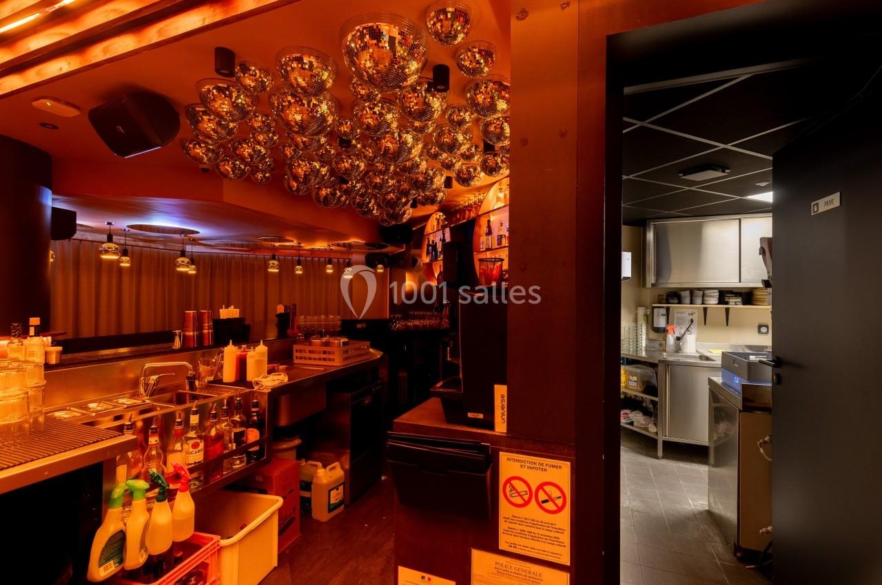 Intérieur d'un bar avec comptoir équipé, éclairage chaleureux et accès visible à une cuisine professionnelle.