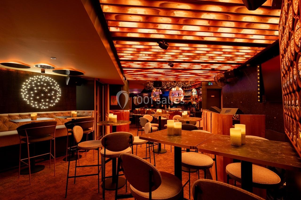 Salle de bar avec éclairage chaleureux, tables hautes, chaises rembourrées et décorations lumineuses au plafond.