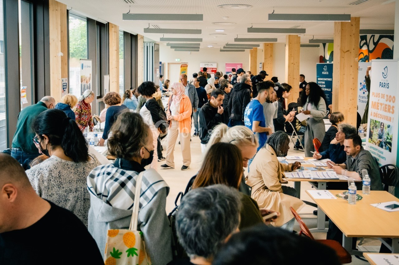 Des personnes participent à un forum ou événement dans une salle lumineuse avec des stands et des discussions en cours.