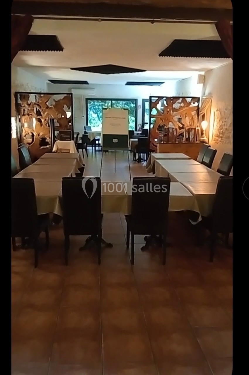 Salle de réunion avec tables rectangulaires disposées en U, chaises noires et décorations murales en bois ajouré.