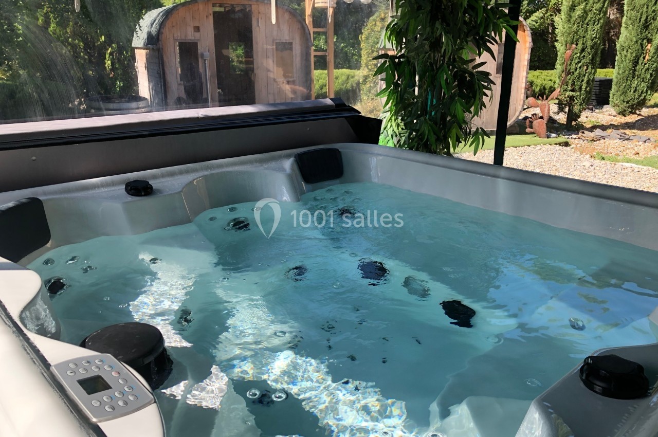 Bain à remous extérieur avec eau claire, entouré de verdure et d'une cabane en bois en arrière-plan.