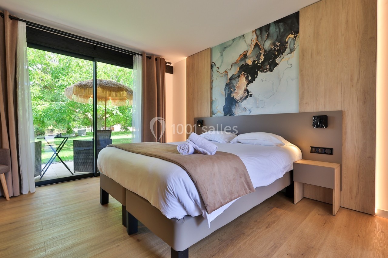 Chambre lumineuse avec un lit double, une grande baie vitrée donnant sur un jardin et une décoration moderne.