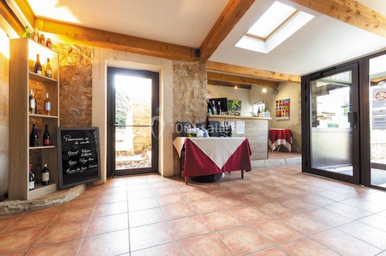 Intérieur lumineux avec murs en pierre, étagère de bouteilles, table dressée et portes vitrées donnant sur l'extérieur.