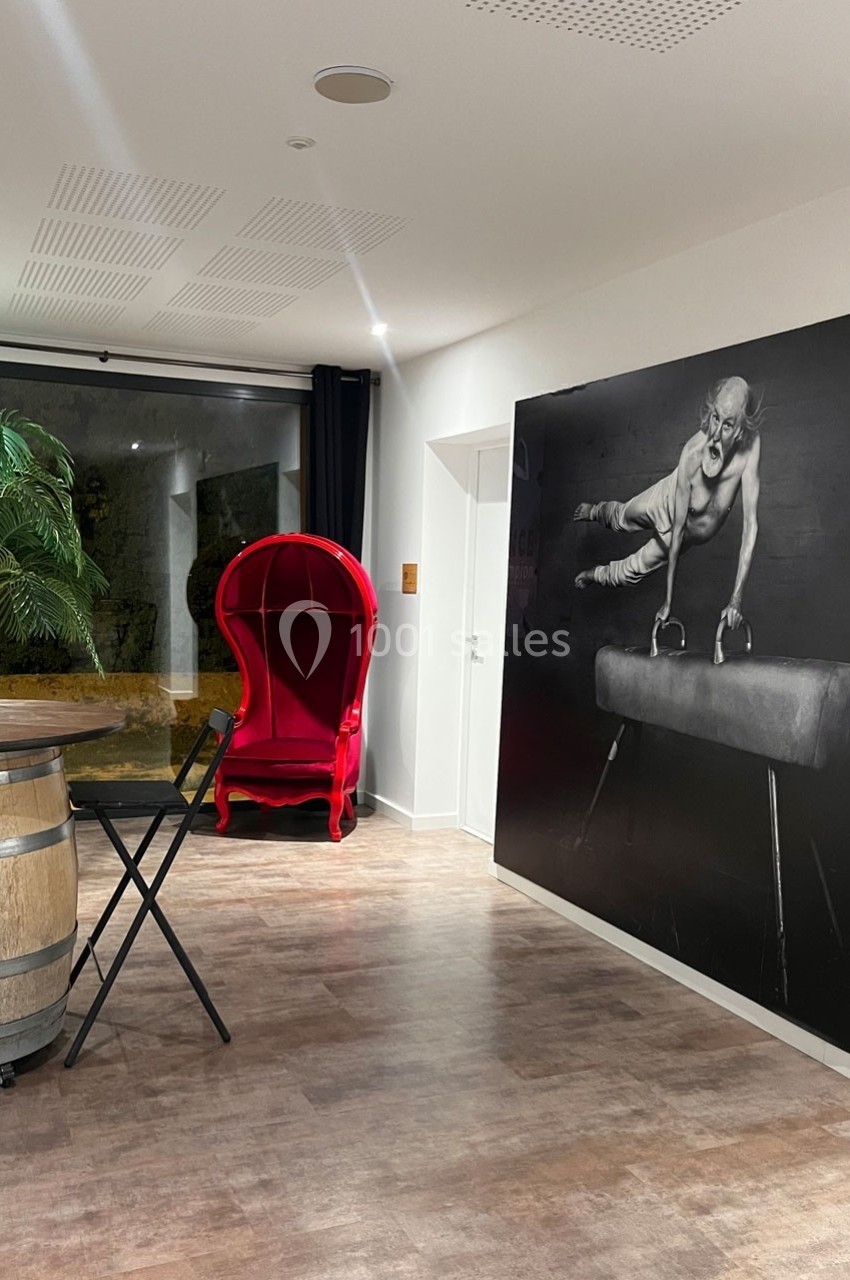 Salle moderne avec un fauteuil rouge, un tonneau en bois, une table pliante et une grande photo en noir et blanc au mur.