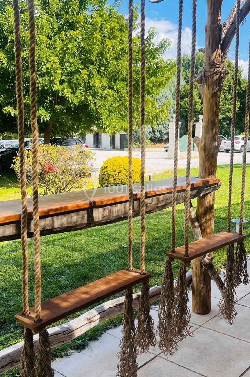 Deux balançoires en bois suspendues à des cordes, installées sur une terrasse avec vue sur un jardin verdoyant.