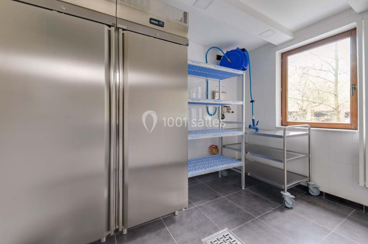 Cuisine professionnelle avec réfrigérateur en acier inoxydable, étagères métalliques et fenêtre laissant entrer la lumière…