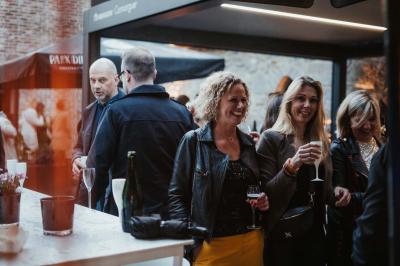 Des personnes discutent debout dans un espace extérieur, entourées de verdure et de mobilier de jardin.