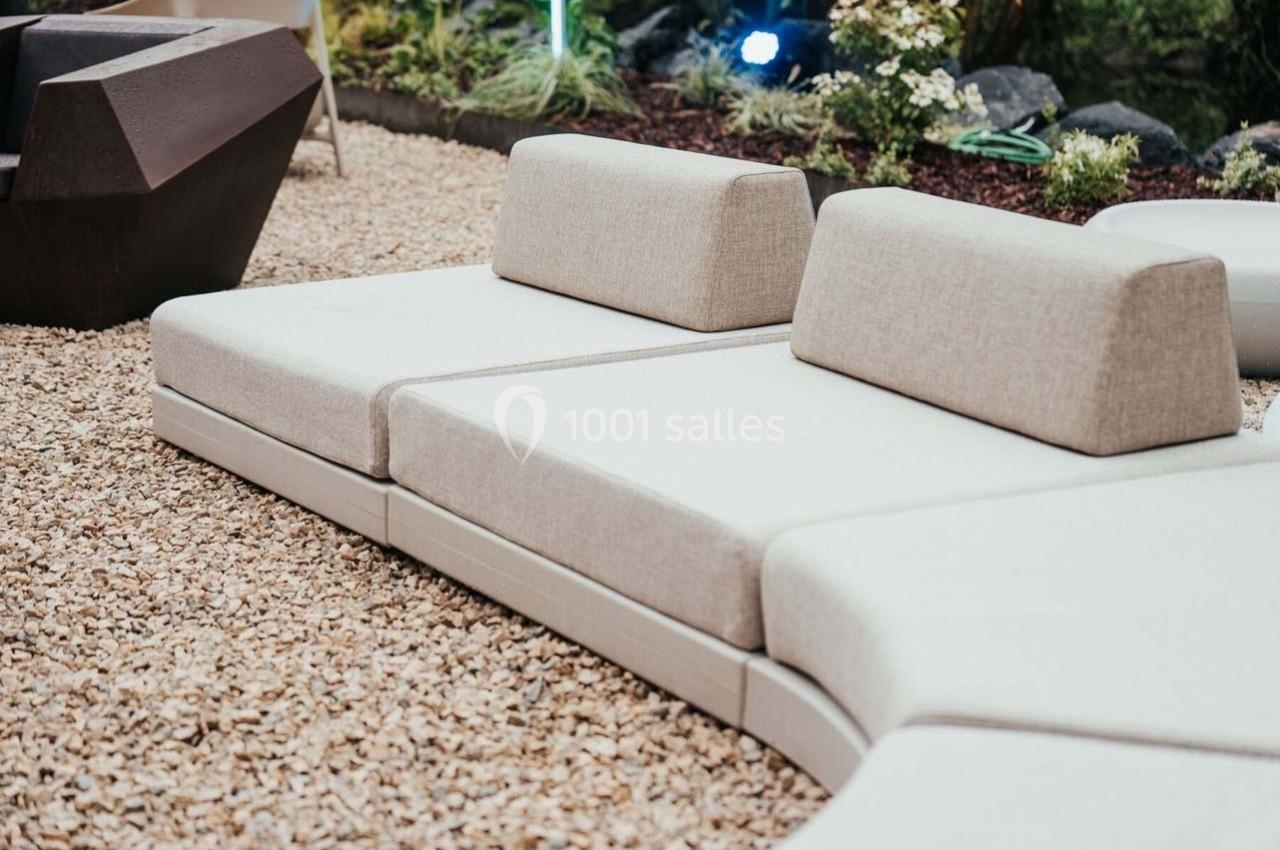 Canapés modulables beige clair disposés sur un sol en gravier dans un espace extérieur aménagé avec des plantes.
