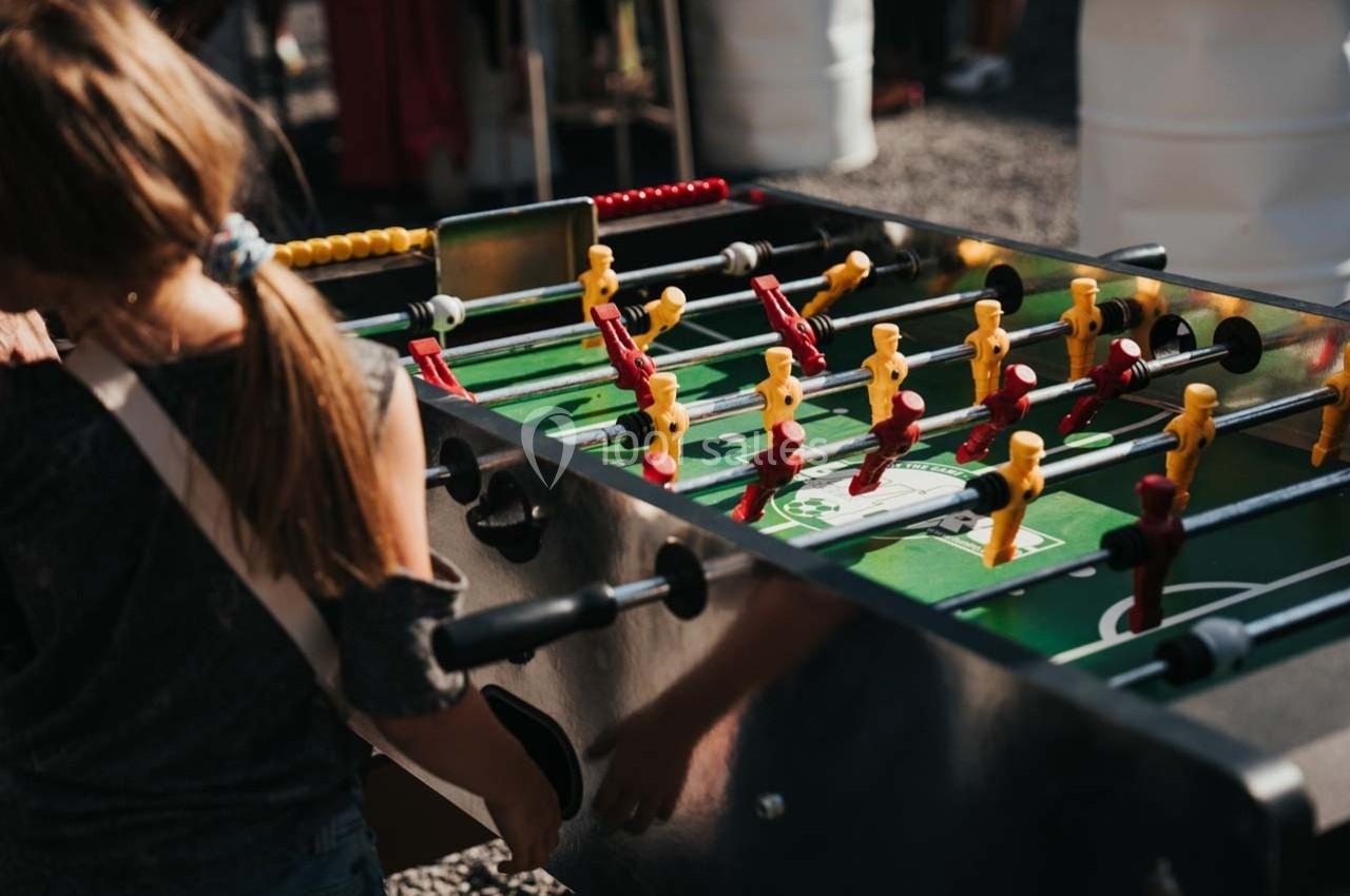Une enfant joue sur un baby-foot en extérieur, entourée d'autres personnes.
