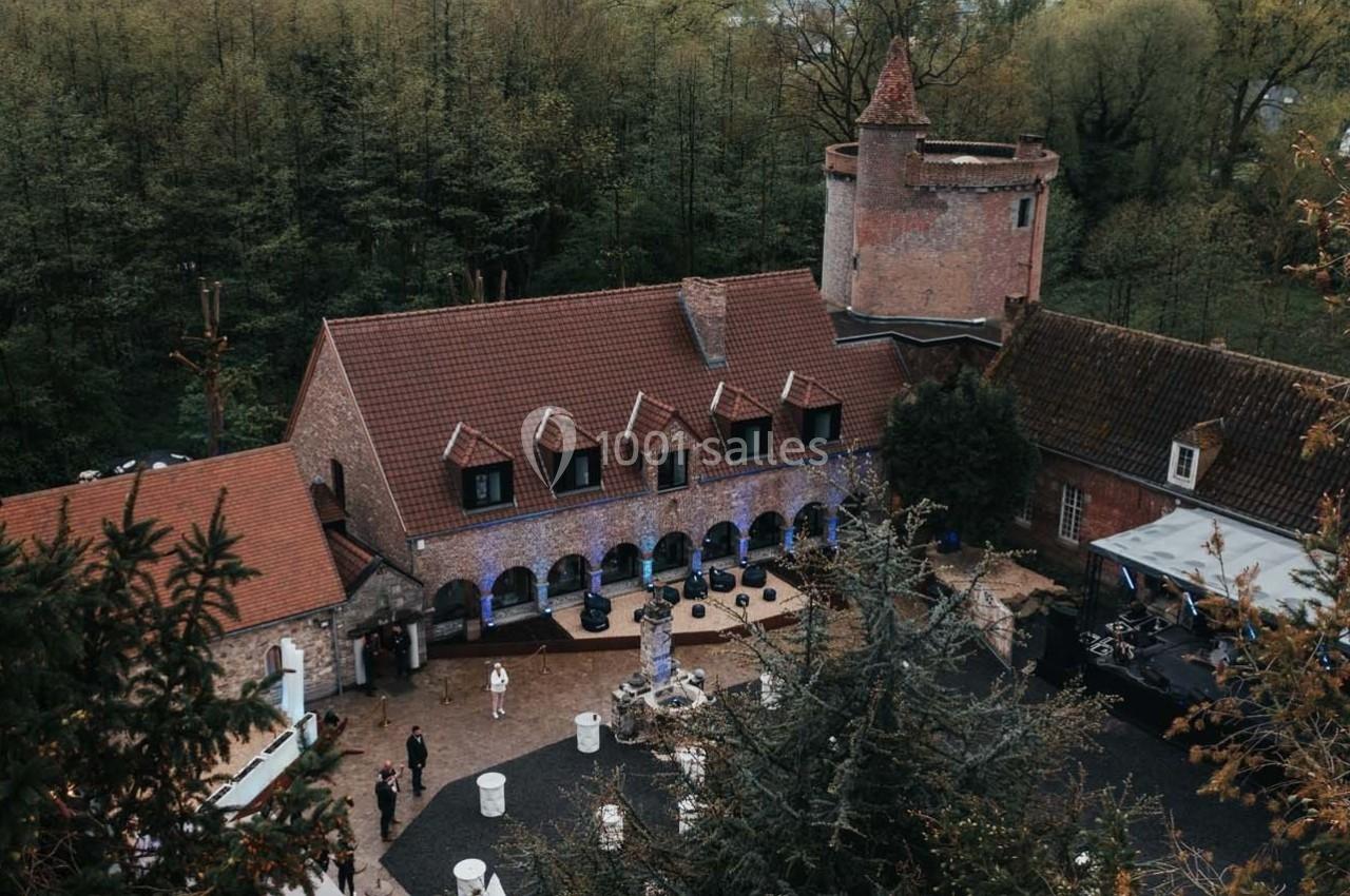 Vue aérienne d'un bâtiment en briques avec une tour, entouré d'arbres et d'une cour aménagée pour un événement.