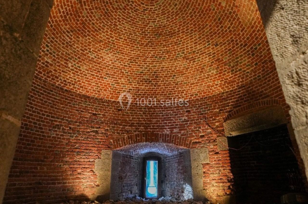 Intérieur d'une pièce voûtée en briques rouges avec une petite ouverture laissant passer la lumière naturelle.