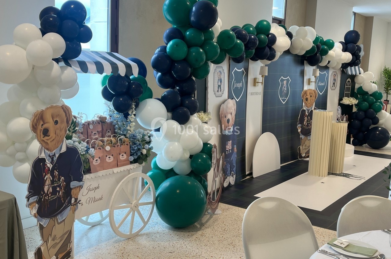 Décoration de fête avec ballons verts, blancs et bleus, et panneaux illustrant des ours en tenue élégante.