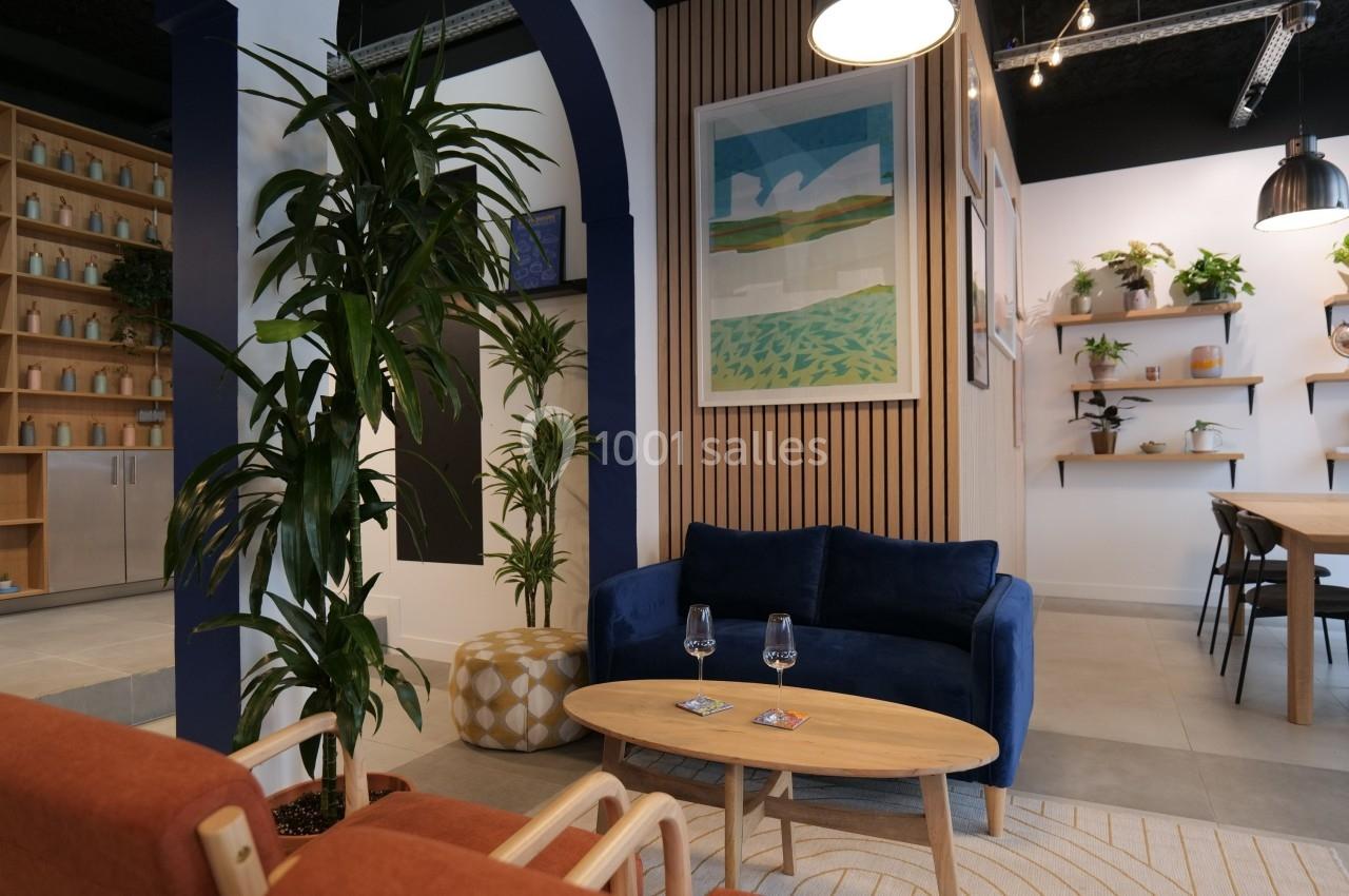 Espace intérieur moderne avec canapé bleu, plantes décoratives, étagères murales et table en bois clair.