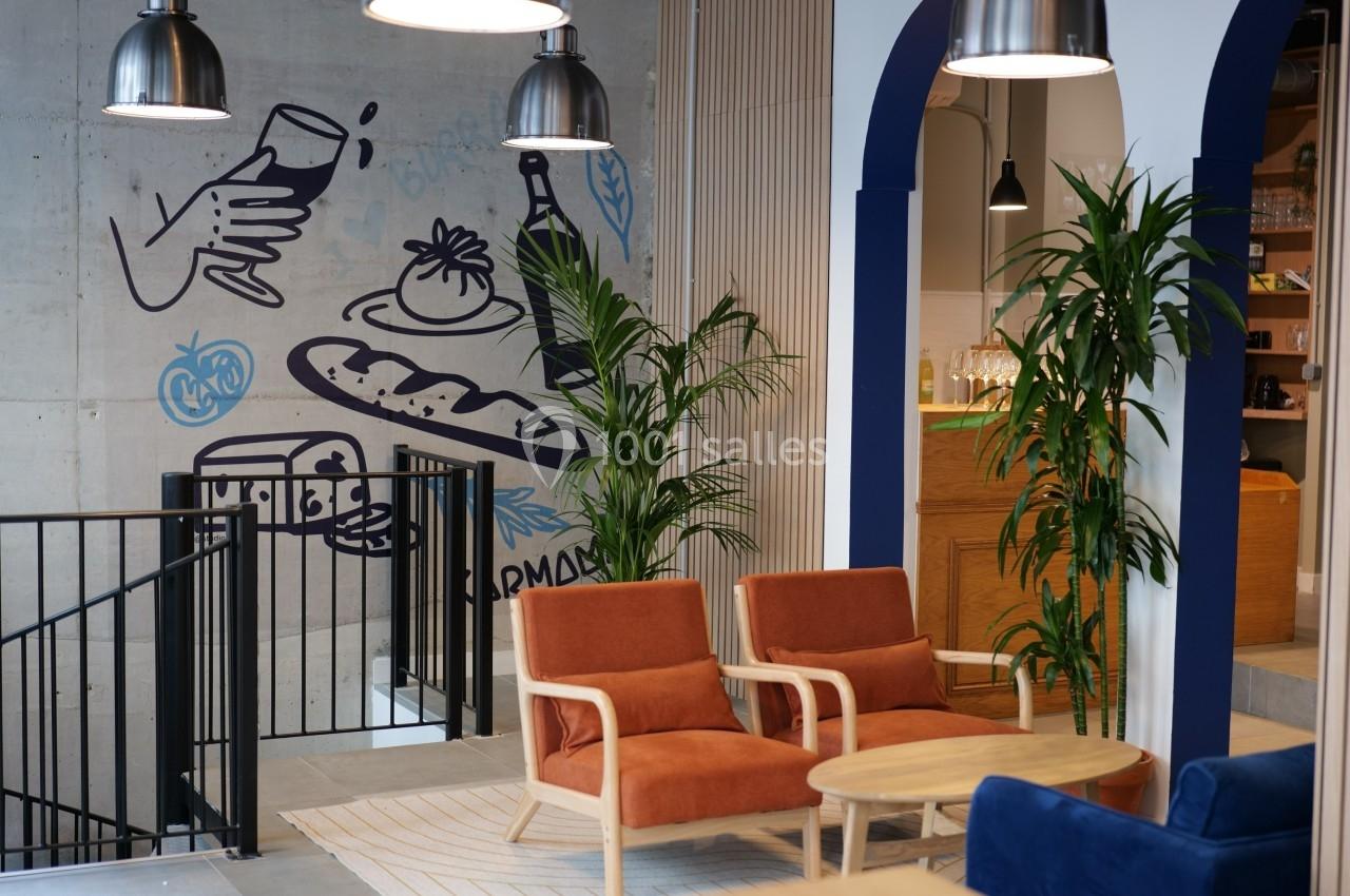 Espace intérieur moderne avec fauteuils orange, plantes vertes et fresque murale illustrant des aliments et boissons.