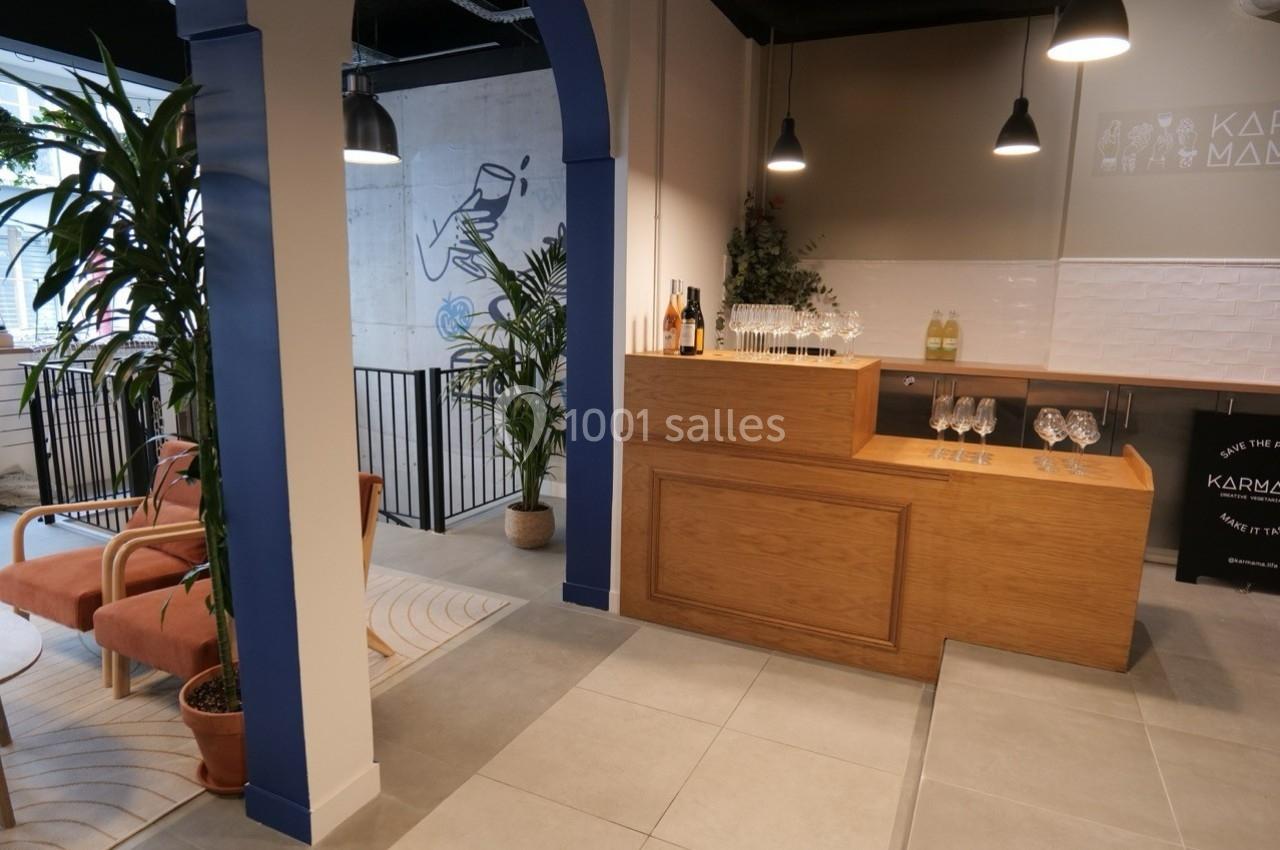 Espace intérieur moderne avec comptoir en bois, chaises, plantes et décoration murale dans un cadre lumineux.