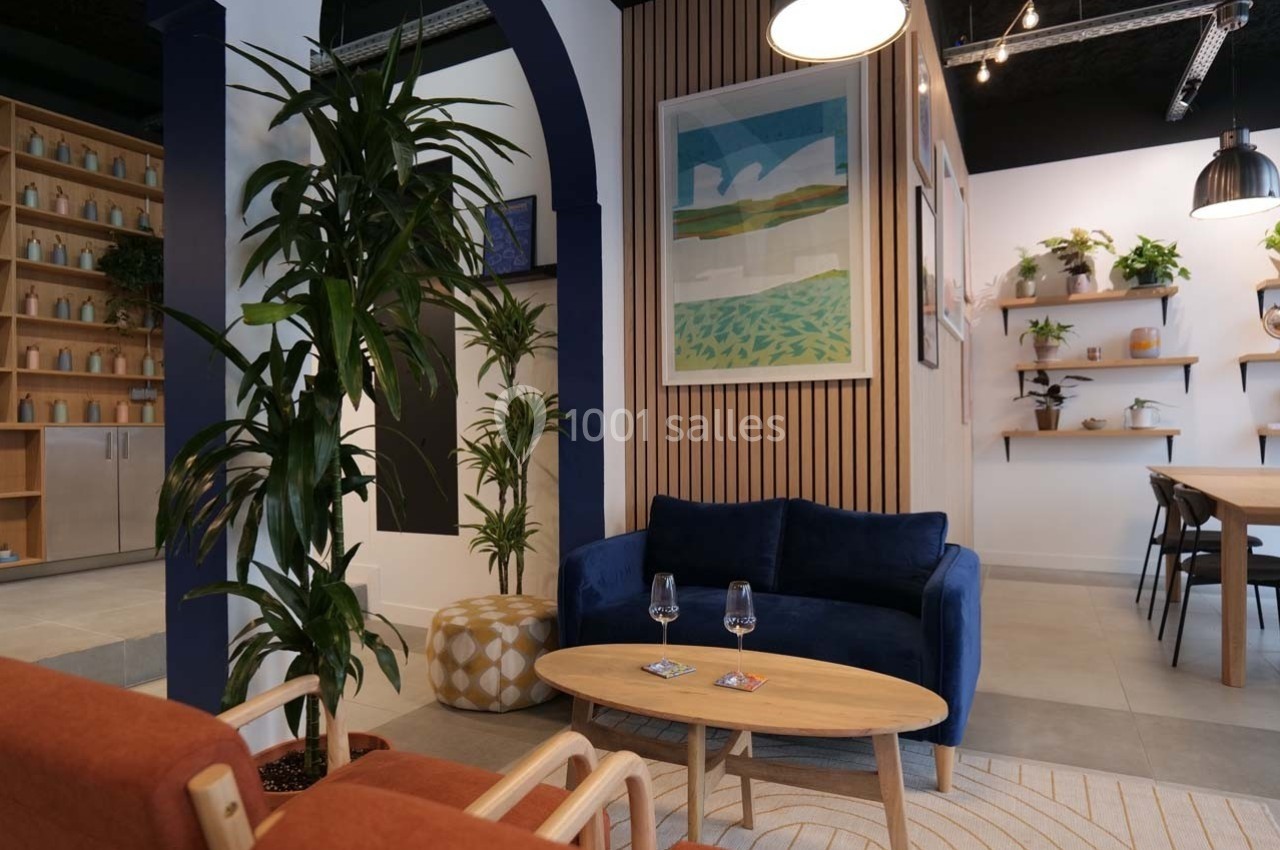 Espace intérieur moderne avec canapé bleu, plantes, table basse en bois et étagères décorées de pots et cadres.