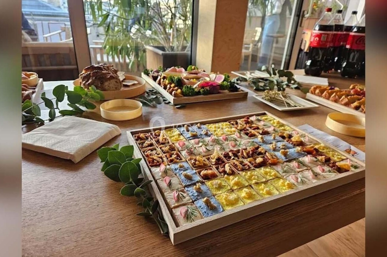 Plateau de bouchées variées colorées sur une table en bois, entouré de boissons et autres plats.