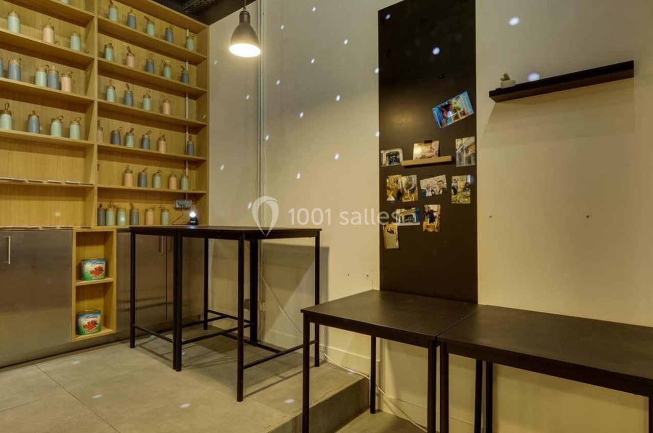 Espace intérieur avec étagères remplies de bouteilles, tables noires et mur décoré de photos sous un éclairage tamisé.