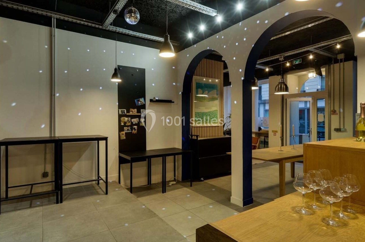 Intérieur d'un espace moderne avec étagères, tables, bouteilles de vin et éclairage tamisé.