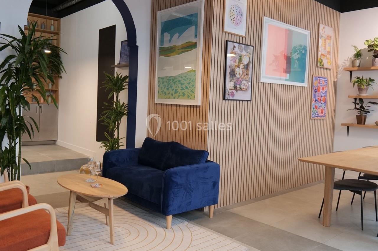 Espace intérieur moderne avec canapé bleu, table basse en bois, plantes et mur décoré de cadres colorés.