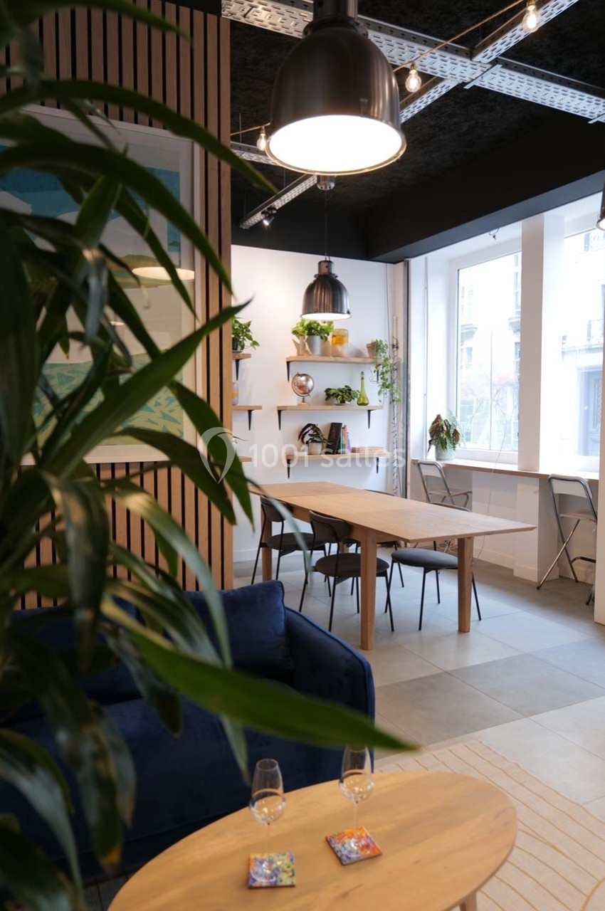 Espace intérieur lumineux avec table en bois, chaises, étagères décorées et plantes, éclairé par des suspensions modernes.