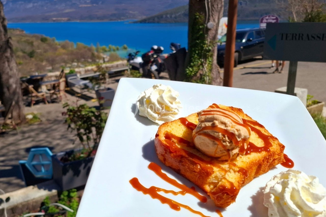 Tranche de brioche perdue avec glace vanille, caramel et chantilly, servie en terrasse avec vue sur un lac et des montagnes.